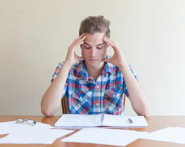 Jonge volwassene studeren, gevoel gefrustreerd, in een rommelig bureaublad Rechtenvrije Stockfoto's