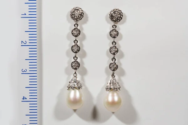 Lång designer Guld örhänge med pärlor och diamanter på en vit bakgrund bredvid linjalen Royaltyfria Stockbilder