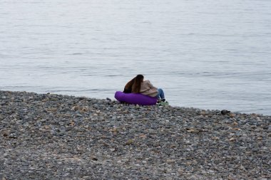 İki arkadaş şezlonglarda oturup denize bakıyorlar. Plajda fasulye koltuğu, ilkbaharın başında.