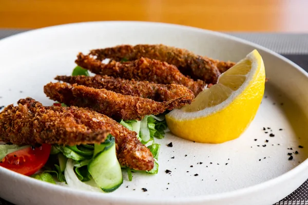 Le poisson frit sentait dans l'assiette, servi avec du citron, des légumes grillés. Éperlan-petit poisson de mer — Photo