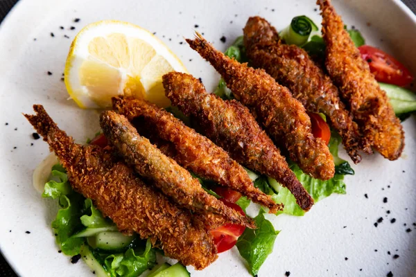 Vue de dessus Poisson frit senti sur l'assiette, servi avec du citron, légumes grillés. Éperlan-petit poisson de mer — Photo
