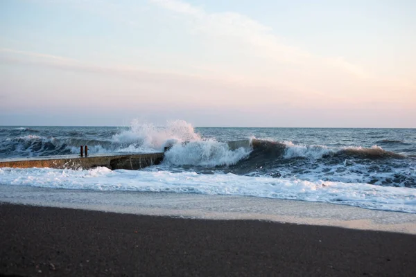 Una tormenta en una playa de arena al amanecer. un paisaje oceánico dramático con un cielo suavemente rosado y olas blancas espumosas. agua tormentosa y olas rompiendo en la luz de la mañana — Foto de Stock