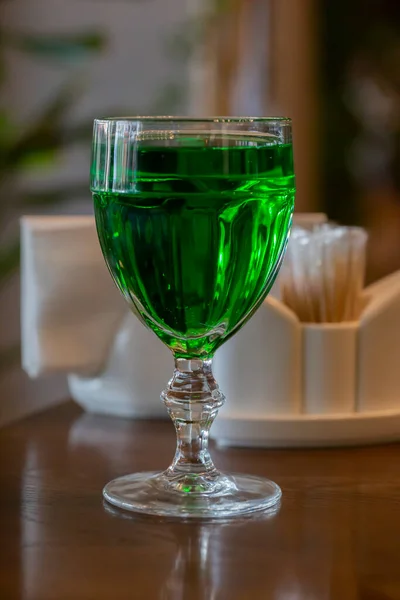 Verre transparent avec une boisson au vin sur une table en bois. Boisson verte lumineuse dans un verre — Photo