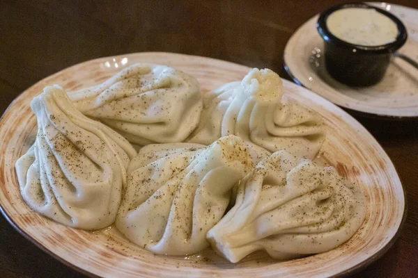Khinkali - traditional Georgian dumplings in a white plate with white sour cream sauce on a wooden table in the restaurant — Stock Photo, Image