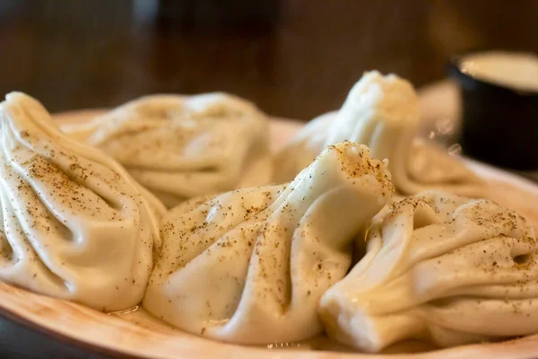 Khinkali - traditional Georgian dumplings in a white plate with white sour cream sauce on a wooden table in the restaurant — 图库照片