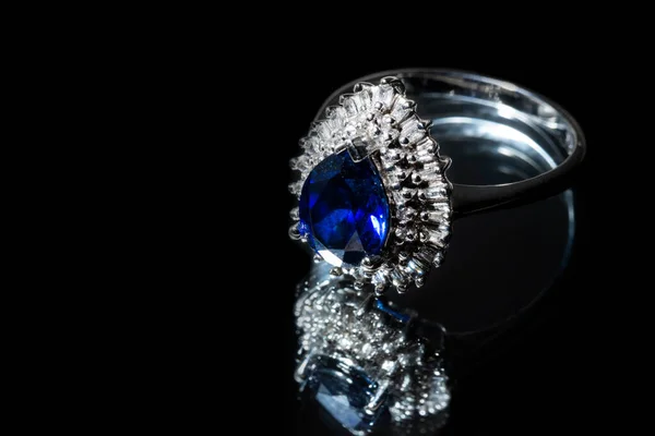 Smycken guld ring med en stor blå safir och diamanter på en svart bakgrund med reflektion Stockbild