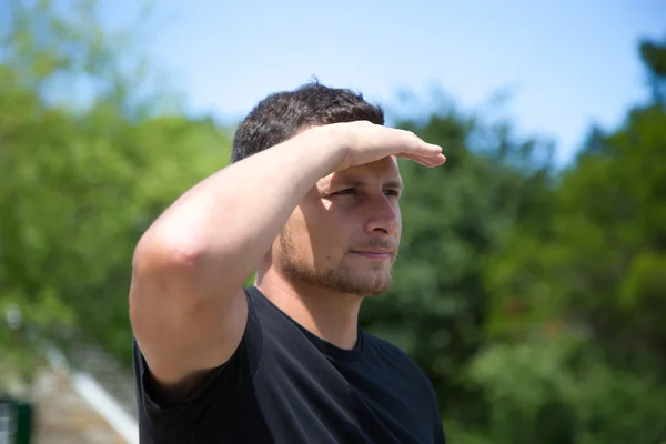 Young man looking out with hand over eyes