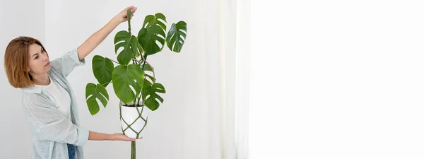Cabides de planta macrame verde artesanal com planta em vaso estão pendurados na mão da mulher. vaso e planta monstera — Fotografia de Stock