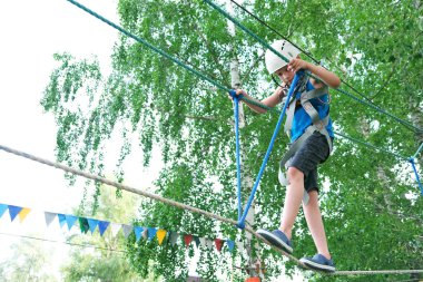 Çocuk yaz eğlencesini teleferik hattındaki macera parkında yapıyor. Denge ışını ve halat köprüleri