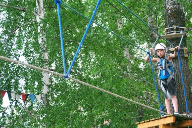 Çocuk yaz eğlencesini teleferik hattındaki macera parkında yapıyor. Denge ışını ve halat köprüleri