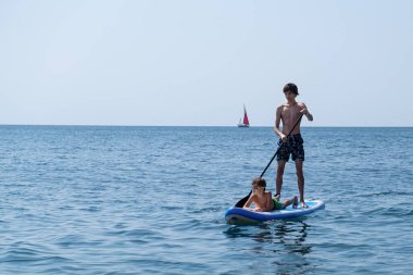 Çocuklu genç bir sporcu denizde sup ile denize açılır. Sağlıklı yaşam tarzı kavramı