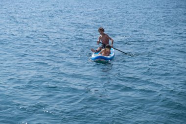 Çocuklu genç bir sporcu denizde sup ile denize açılır. Sağlıklı yaşam tarzı kavramı