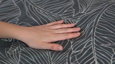Kadın avuç içi, yatak odasındaki gri pamuklu yatak çarşaflarına dokunuyor. Ev içi çarşaf..