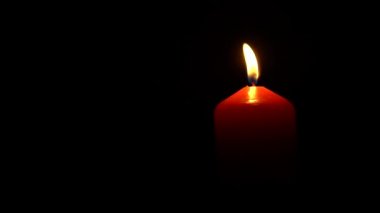Siyah bir arka planda tek bir büyük kırmızı mum alevi var. Dua, umut ve yas kavramı.