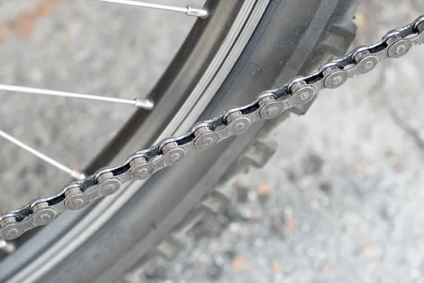 Dark metallic chain of a Bicycle filmed in close up. Small details are visible. The background is blurred.