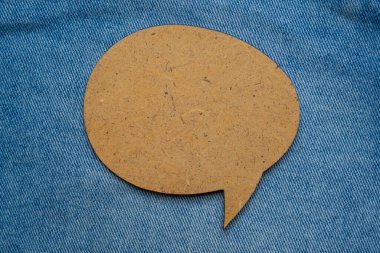 Wooden speech bubble balloon label on jeans background with shadow. Blank speech bubble on cloth background.