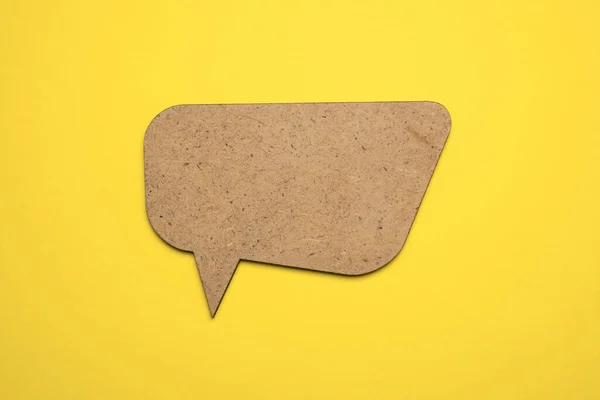 Brown wood speech bubble on yellow paper. Close up of paper blank speech bubble, isolated on yellow background with copy space for advertisement. Mockup.