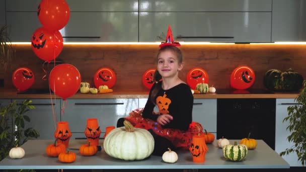 Een meisje in een heksenkostuum maakt de kijker bang op Halloween. ballonnen, pompoenen. — Stockvideo