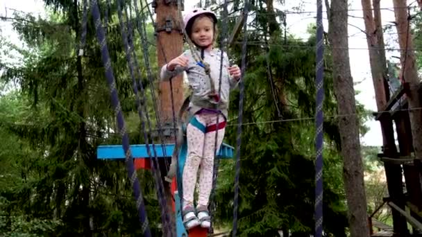 Una chica se mueve en los parques de cuerdas colgando de un sendero a una altura entre los árboles — Vídeos de Stock