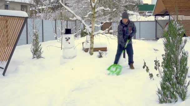 Ένας ώριμος άντρας καθαρίζει το μονοπάτι κοντά στο σπίτι από το χιόνι κατά τη διάρκεια έντονης χιονοθύελλας. χιονάνθρωπος — Αρχείο Βίντεο