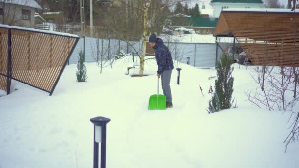 Ένας ώριμος άντρας καθαρίζει το μονοπάτι κοντά στο σπίτι από το χιόνι κατά τη διάρκεια έντονης χιονοθύελλας. χιονοστιβάδες — Αρχείο Βίντεο