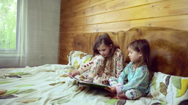 Zwei lächelnde Vorschulkinder lesen im Schlafanzug ein großes, interessantes Buch.. — Stockvideo