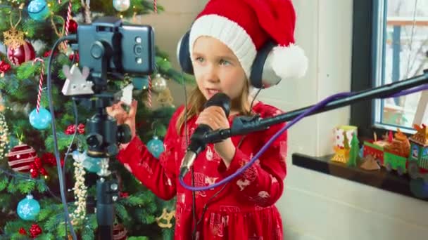 Ovlivňující dívka v klobouku Santa Clause zpívá píseň do mikrofonu. blogger girl — Stock video