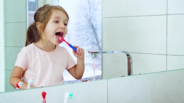 Dívka si čistí zuby a jazyk u velkého zrcadla v koupelně. Zubní — Stock video