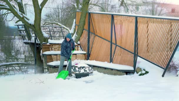 Un hombre adulto limpia los caminos del jardín de la nieve. Paleando nieve de los caminos — Vídeo de stock