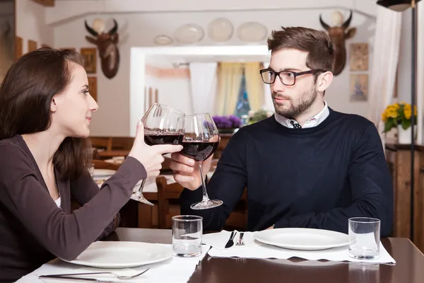 Улыбающийся молодой человек, звенящий в очках со своей девушкой за ужином — стоковое фото