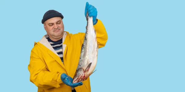 Visser in een geel pak houdt een vers gevangen vis in zijn handen. vanger in de regenjas. — Stockfoto