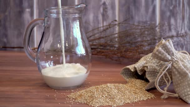 キノアの穀物と牛乳を木のテーブルの上に撒き散らしました チェノポディウムキノア キノアのミルク 柔軟性のある飲み物タンパク質の振動 天然のミネラルやビタミンの複合体は — ストック動画