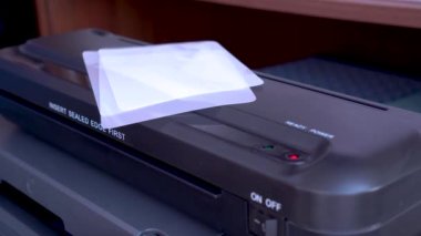 Laminator 'ün işi. Yakın plan, seçici odaklanma. Belgelere, fotoğraflara şeffaf bir film uygulamak için bir cihaz. Bu cihaz, onları tozdan, nemden ve diğer dış etkilerden korur..