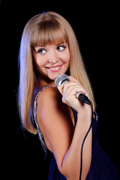 Una encantadora joven rubia sobre un fondo negro con un micrófono —  Fotos de Stock