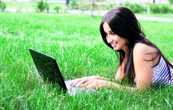 Affascinante bruna con un computer portatile nel prato estivo — Foto Stock