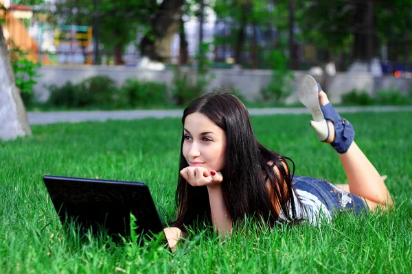 Charmiga brunett med en laptop i sommar ängen — Stockfoto