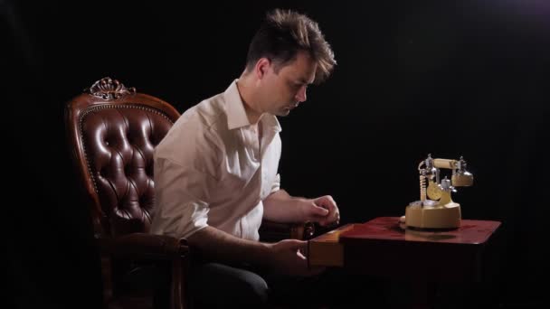 A man on black in a white shirt sits in a chair — Vídeo de stock