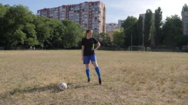 Kız futbolcu, terk edilmiş bir sahada dururken bileğini ovuyor.