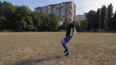 Kız futbolcu topu iki kez dizlerinin üzerine çökerek dolduruyor ve sonra çerçeveden fırlıyor.