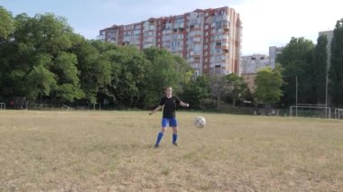 Kız futbolcu topu kenara itiyor ve çimenli bir futbol sahasında onun peşinden koşuyor.