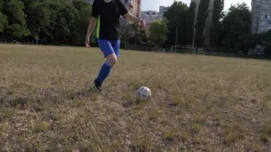 Tozlu bir kız futbol topunu çimenli bir arazide gezdiriyor.