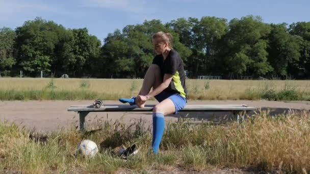 女子サッカー選手はサッカー場を背景にベンチに座って脚を引っ張り — ストック動画