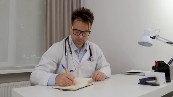 Ein Mann Arztkittel Schreibt Etwas Ein Notizbuch Mit Einem Stift — Stockvideo