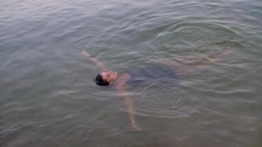 Siyah elbiseli bir kız kollarını açmış suya uzanıyor.