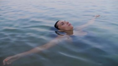 Kollarını açmış suya uzanan ve sonra başını suyun altına indiren bir kızın portresi.