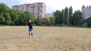 girl footballer dribbles the ball across an abandoned, not well-groomed football field