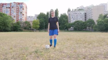the girl looks at the camera and steps on the soccer ball with her foot