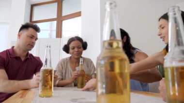 friends of different ethnicity and age group drinking beer at the table and playing cards