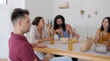 a group of 5 friends are sitting at a table, talking when suddenly one of the guys exclaims sharply and raises his hands to drink for his birthday, clinking bottles of beer