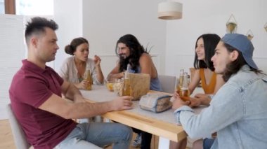 a group of 5 friends are sitting at a table, talking when suddenly one of the guys exclaims sharply and raises his hands to drink for his birthday, clinking bottles of beer